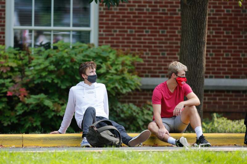 two men sitting on a curb wearing face masks