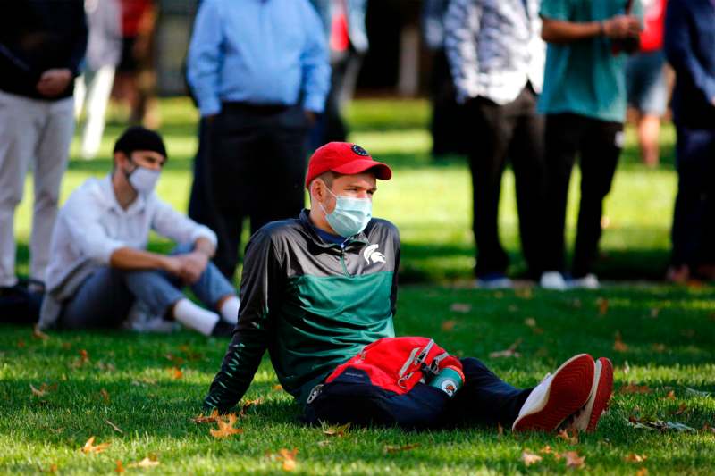 a man sitting on the grass wearing a face mask