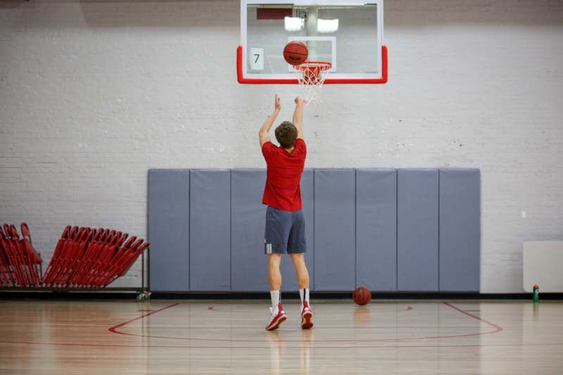 a man in a red shirt and shorts jumping to dunk a basketball