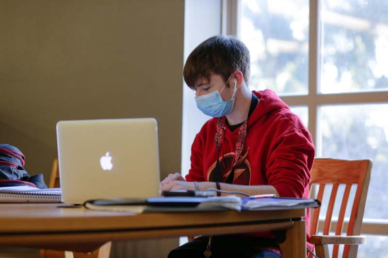 a man wearing a face mask sitting at a desk with a laptop