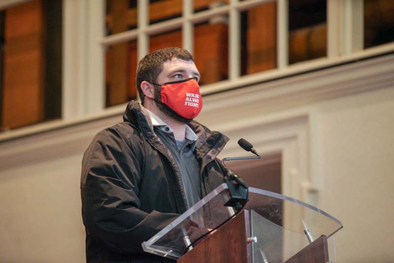 a man standing at a podium with a face mask
