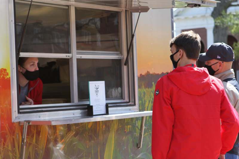a man wearing a mask standing in front of a food truck