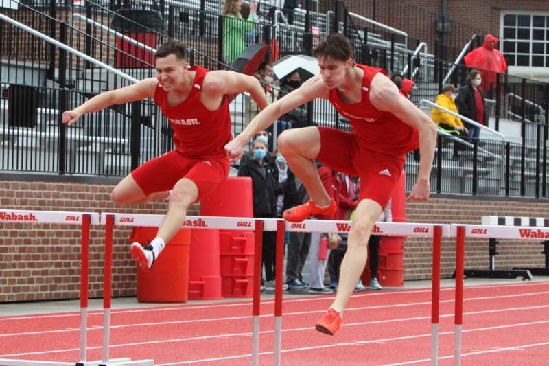 a pair of men jumping over a hurdle