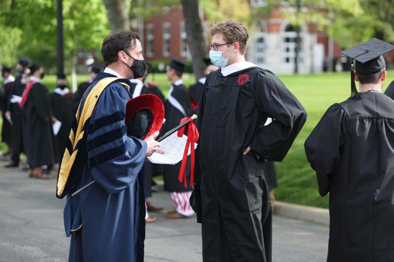 a man wearing a mask and a gown talking to a man in a cap