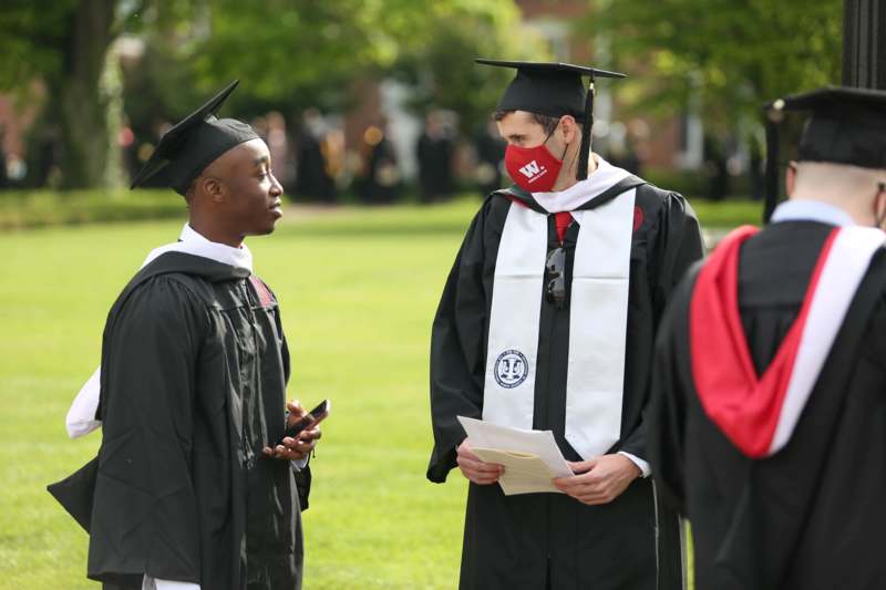 a man wearing a mask and cap and gown standing next to a man wearing a mask
