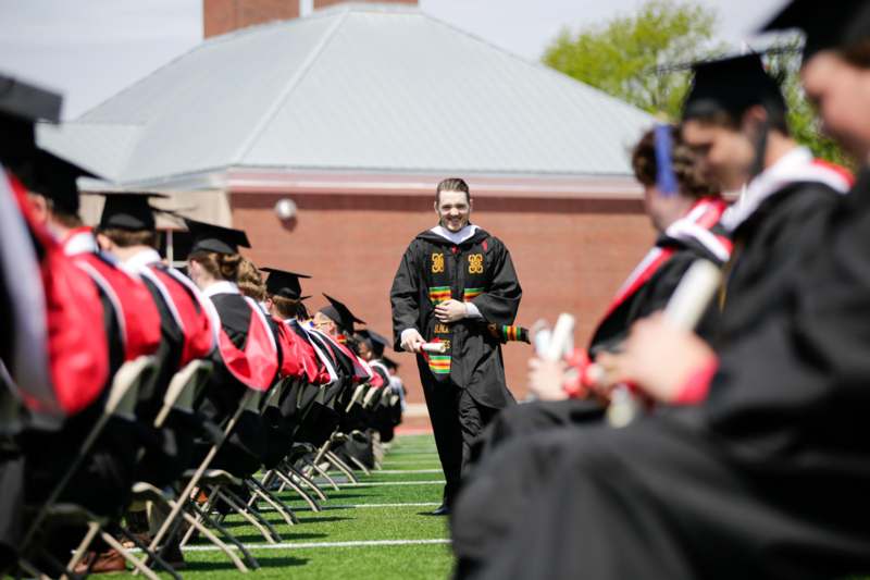 a man in a graduation gown standing in a row of chairs