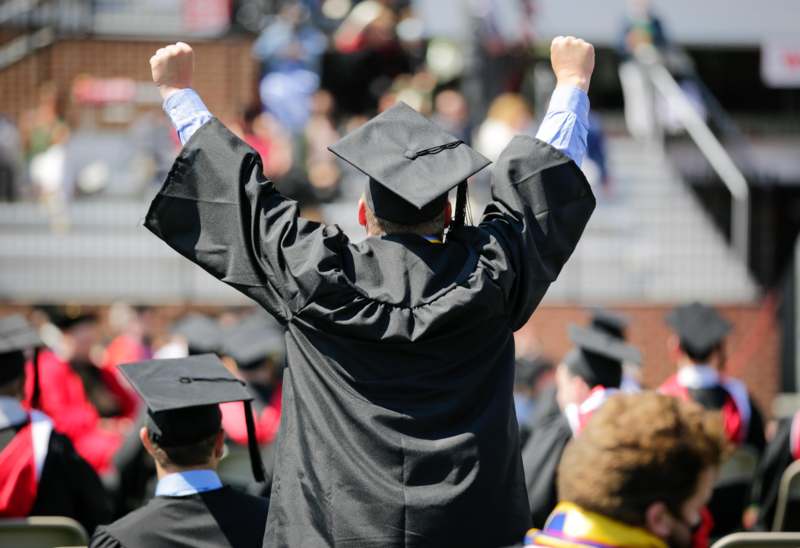 a man in a graduation gown raising his hands