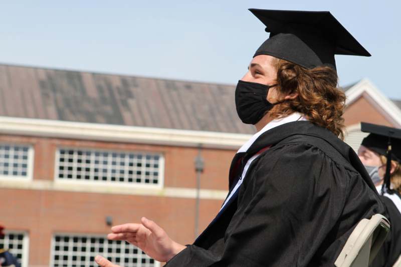 a person wearing a black gown and cap and gown with a face mask