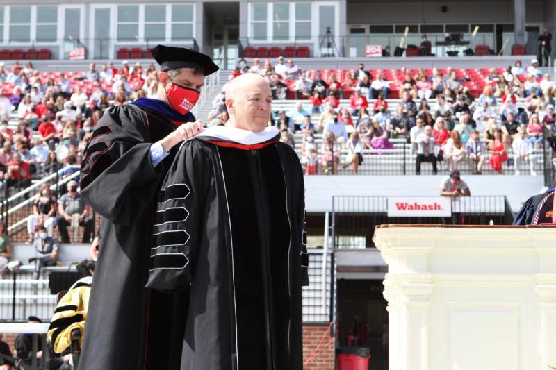 a man wearing a mask and a black gown with a man in a cap and gown