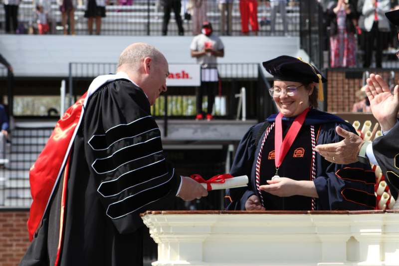a man in a black robe receiving a diploma from a woman
