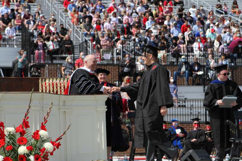 a man shaking hands with a man in a graduation gown