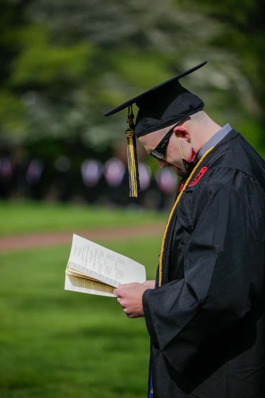 a man in a graduation gown and cap reading a book