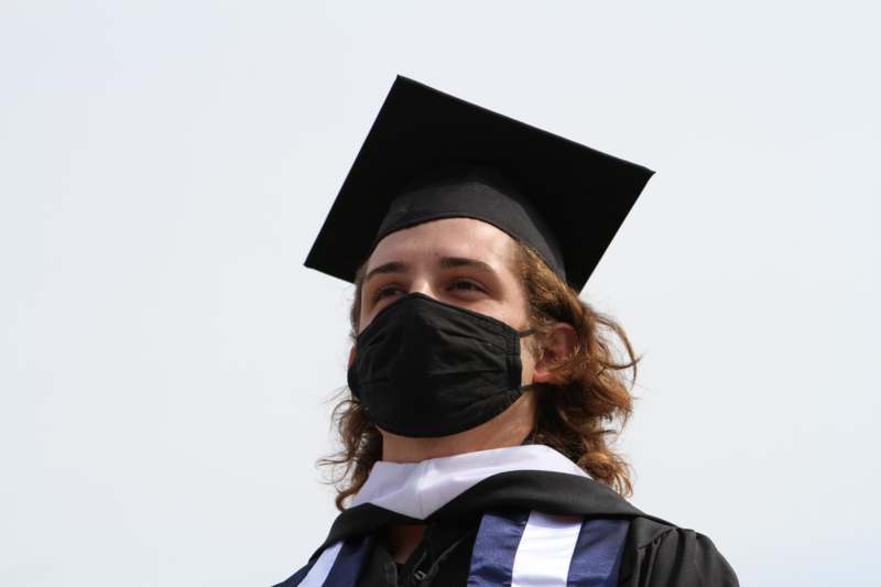 a man wearing a black cap and gown with a black mask