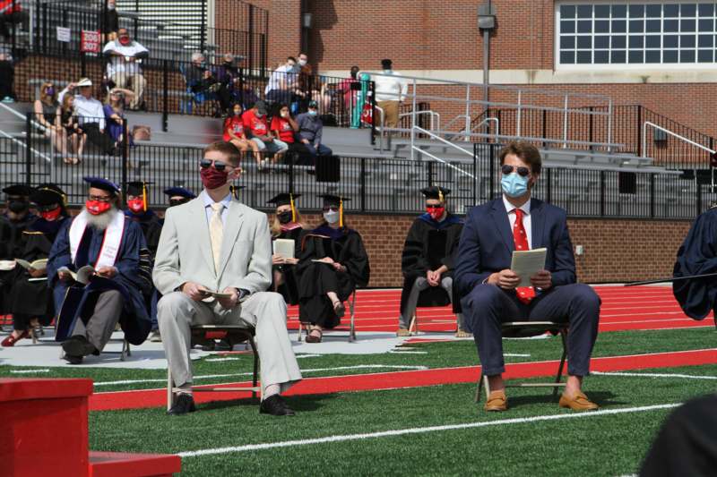 a group of people sitting on a football field wearing masks