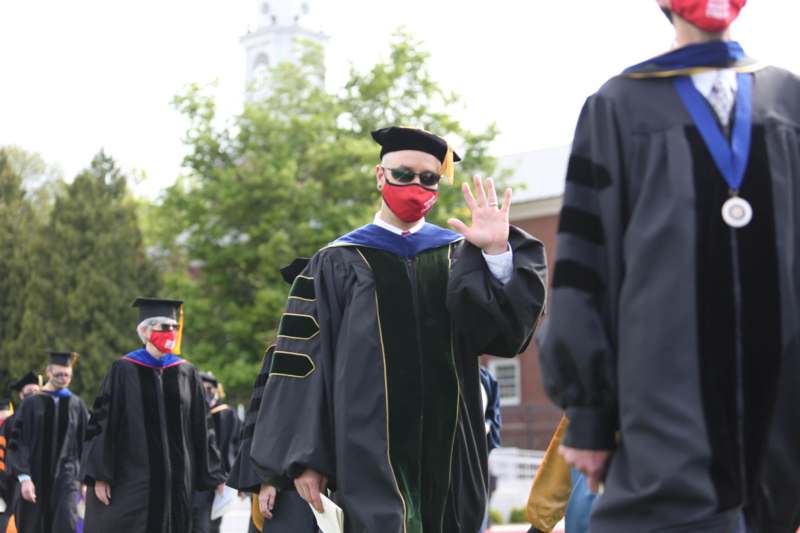a man wearing a mask and cap and gown with other people in the background