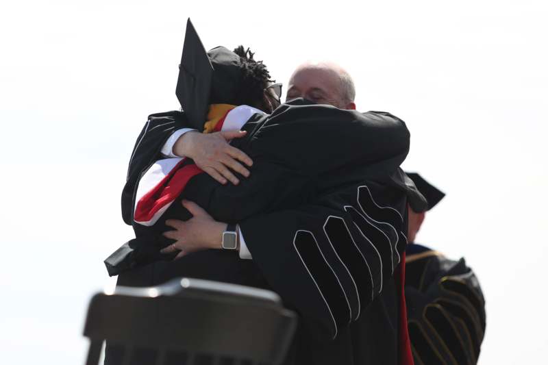 a man in a black robe hugging another man in a black robe