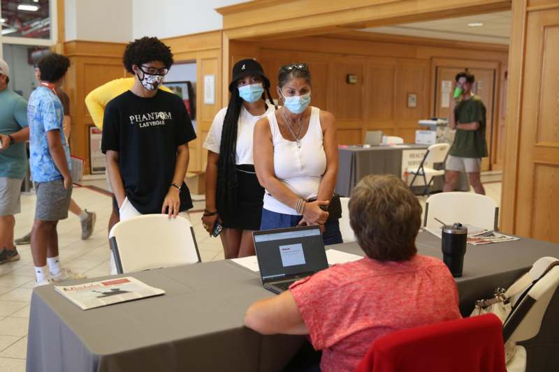 a group of people wearing face masks standing in a room with a laptop