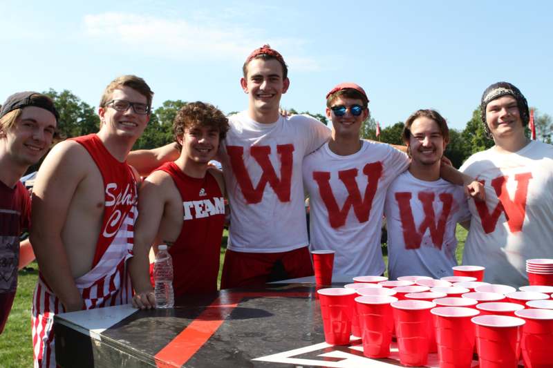 a group of men wearing red shirts and standing next to a table with cups