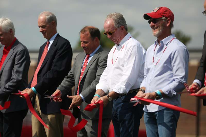 a group of men cutting red ribbon