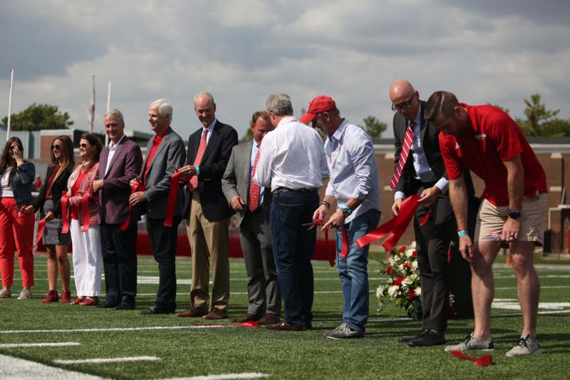 a group of people cutting red ribbons on a football field