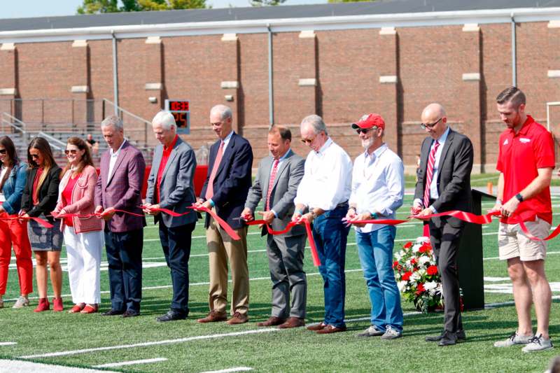 a group of men cutting red ribbon on a football field