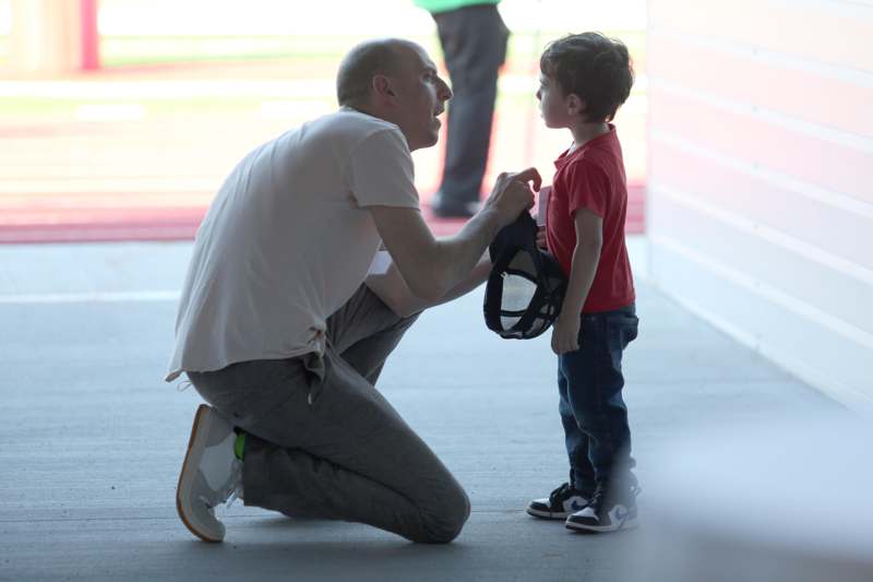 a man kneeling on the ground holding a helmet to a child