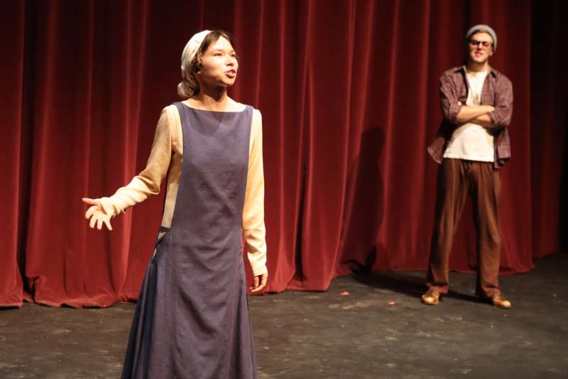 a woman in a dress on a stage with a man in the background