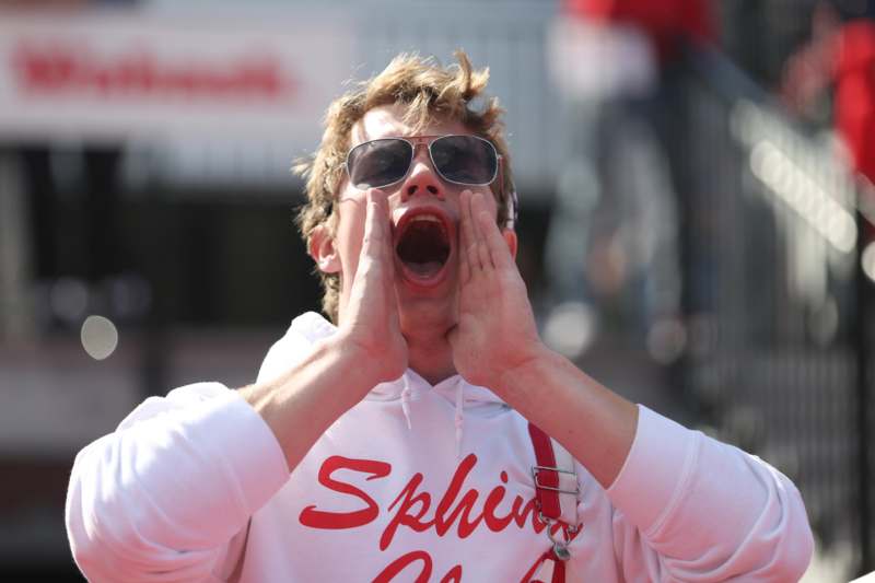 a man wearing sunglasses and a white sweatshirt with his hands in his mouth