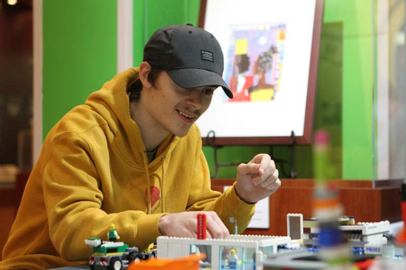 a man wearing a black hat and yellow sweatshirt sitting at a table with legos