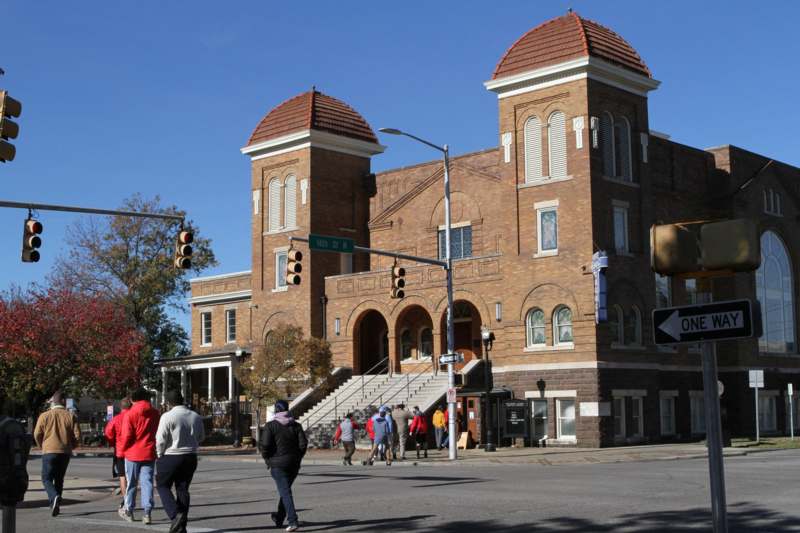 a group of people walking on a street corner with 16th Street Baptist Church in the background
