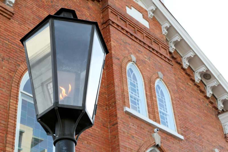 a lamp post with a flame in front of a brick building