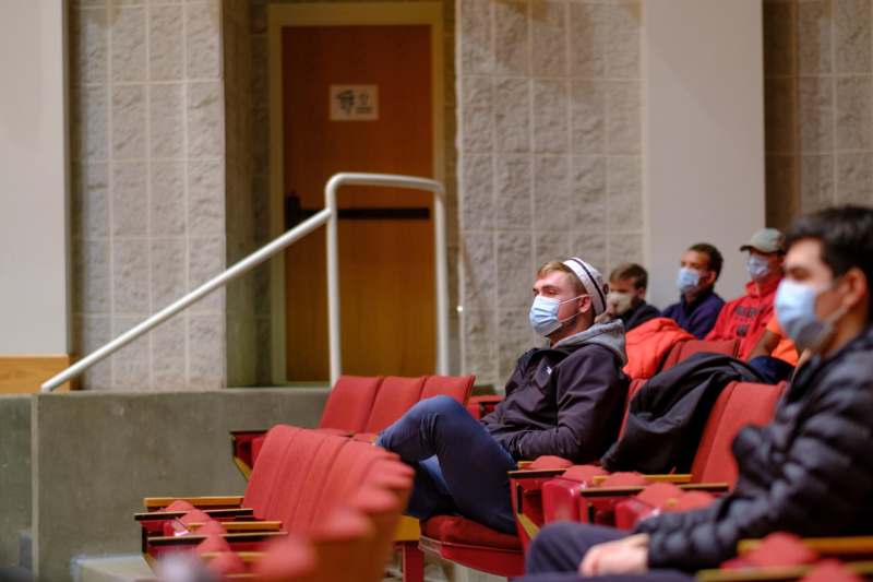 a man wearing a face mask sitting in a auditorium