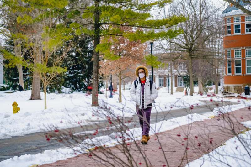 a person wearing a mask walking on a sidewalk in the snow