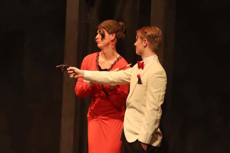 a man in a suit and woman in a red dress holding a gun