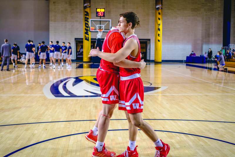 two men in red uniforms hugging on a basketball court