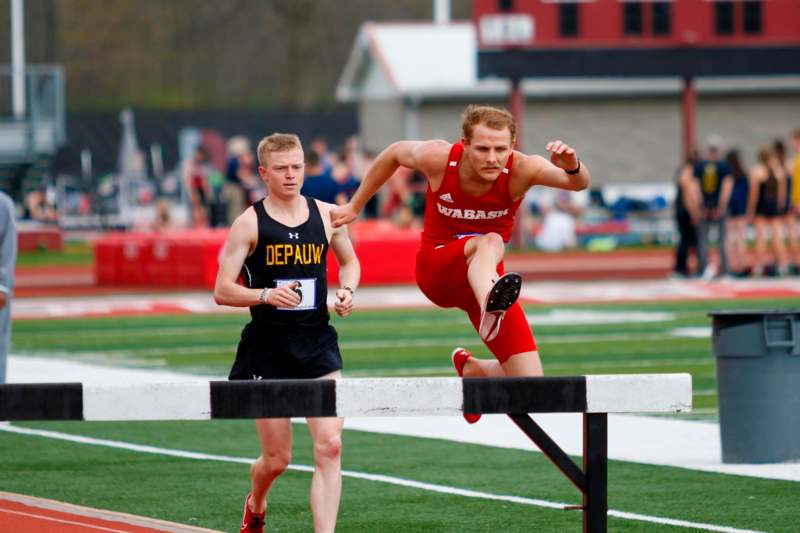 a man in a red shirt running over a hurdle