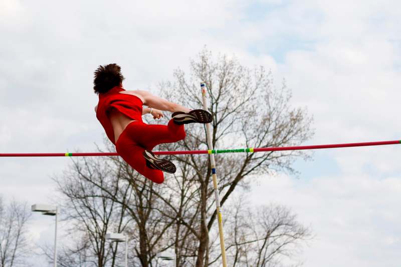 a person in red jumpsuit jumping over a bar