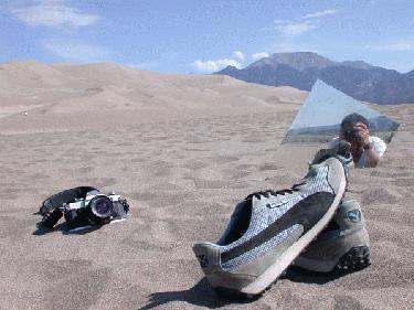 a man sitting on the sand with a camera and a glass