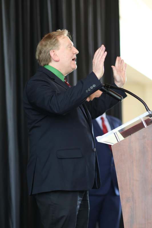 a man in a suit standing at a podium with his hands up