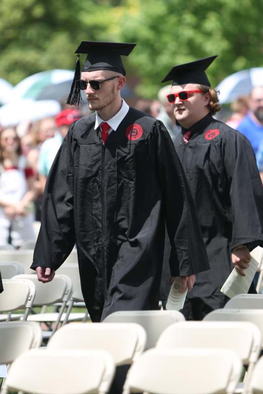 a group of men in graduation gowns and cap and gowns walking in chairs