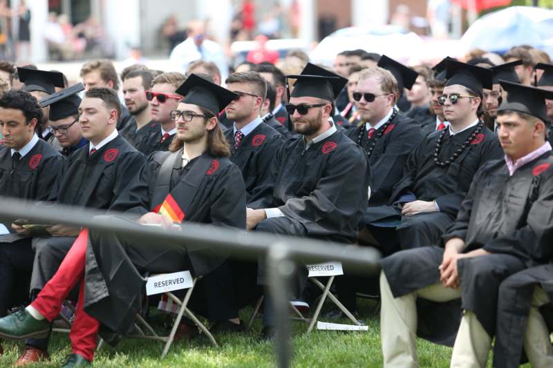 a group of people in graduation gowns and caps sitting on chairs