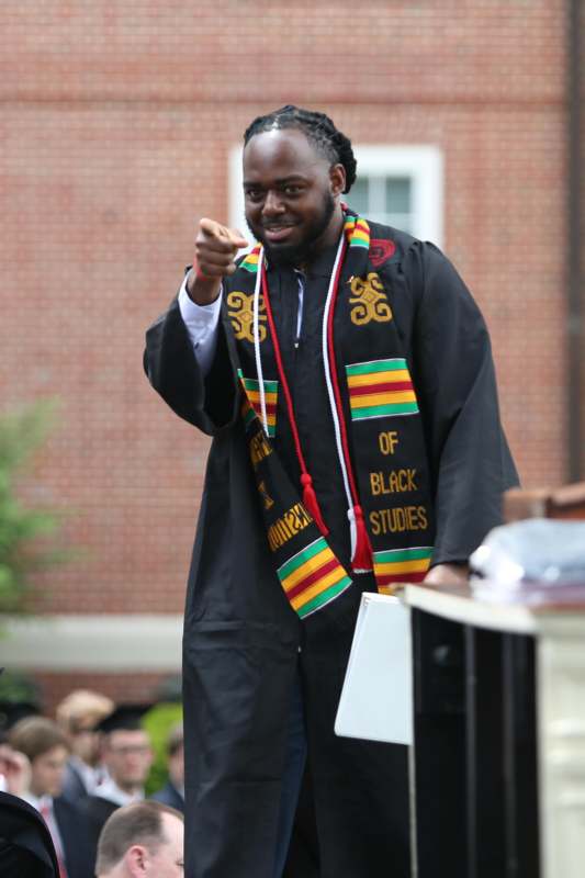 a man wearing a graduation gown pointing at the camera