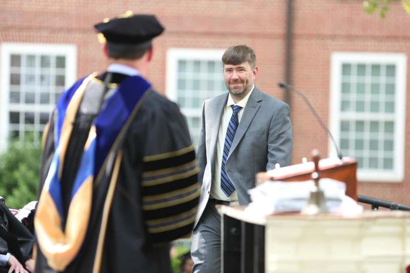 a man in a suit and tie standing in front of a man in a graduation gown