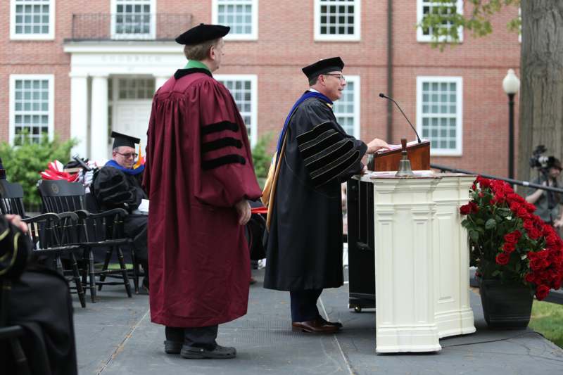 a man in graduation gowns standing at a podium