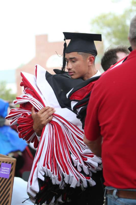 a man in a graduation cap and gown carrying a stack of red and white blankets
