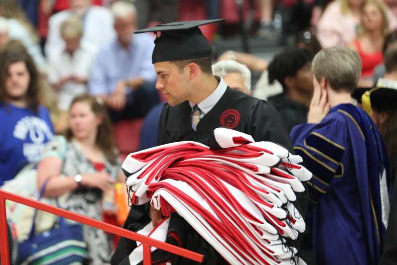 a man in a graduation gown carrying a stack of towels