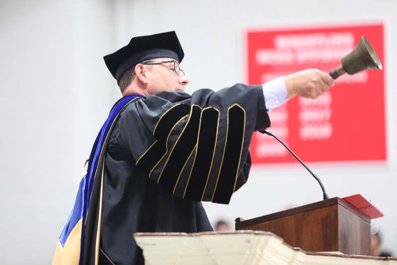 a man in a graduation gown pointing at a microphone
