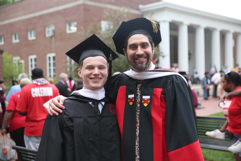a man in a graduation gown and cap with his arm around a man