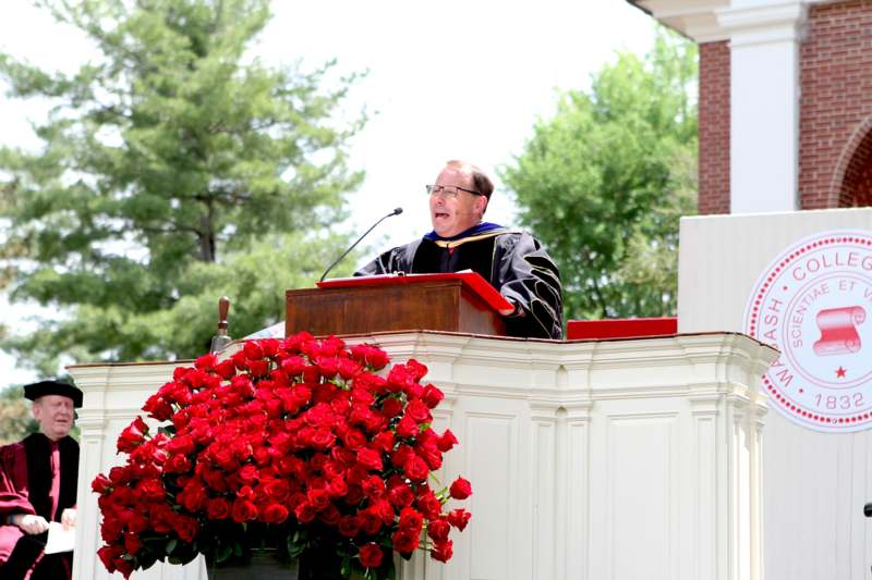 a man in a graduation gown standing at a podium with a microphone