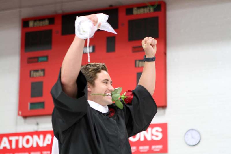 a man in a graduation gown holding a rose and a bag of water